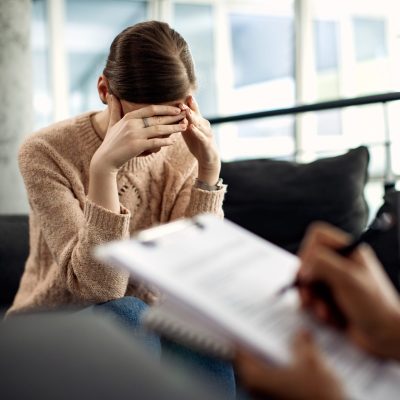 Sad woman holding her head in pain while having a meeting with psychotherapist.